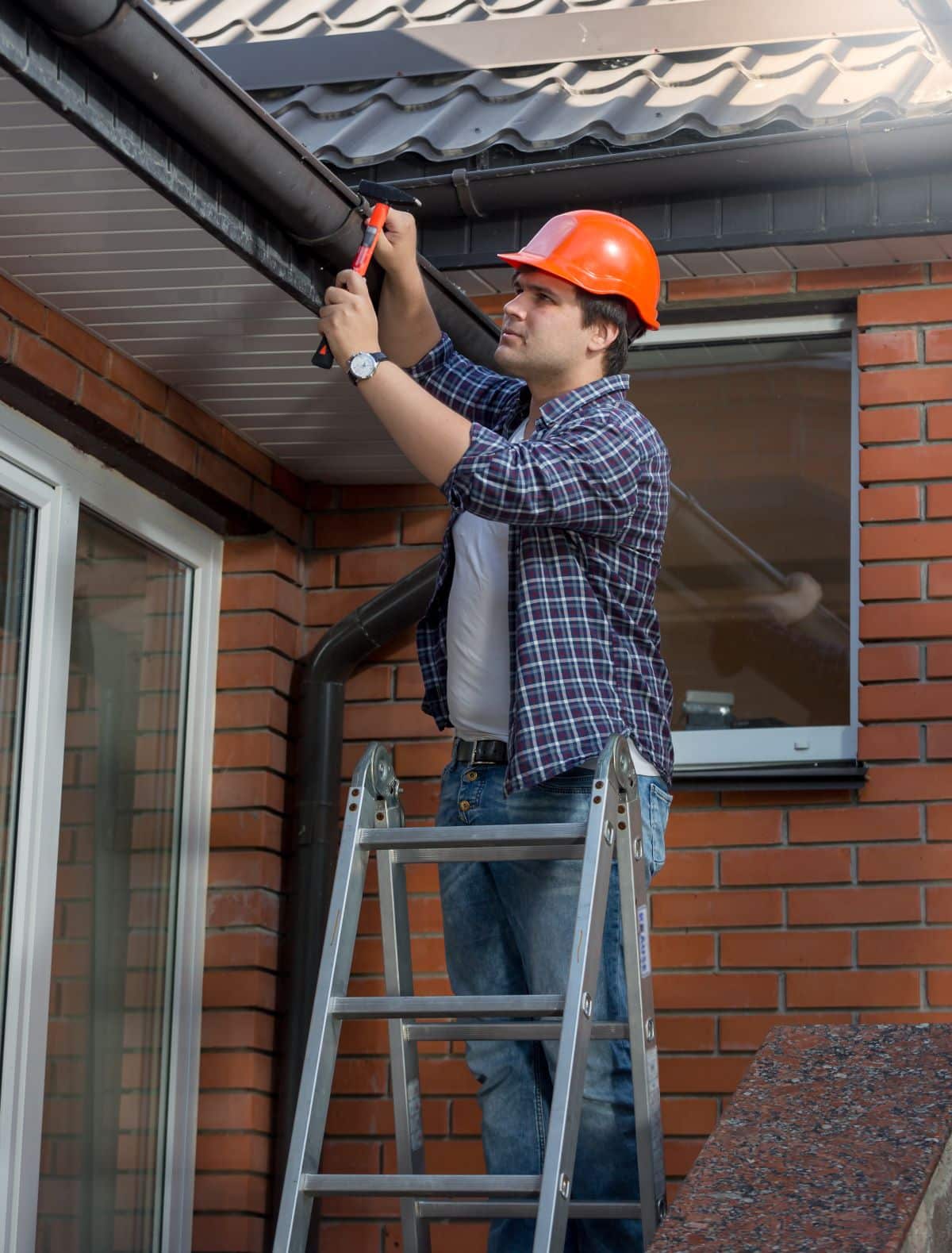 Worker fixing gutter on house roof