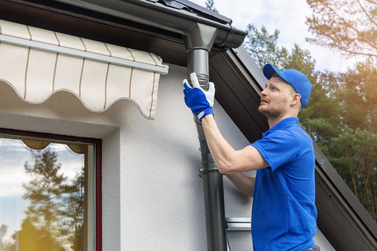 Worker installing house gutter system outdoors.