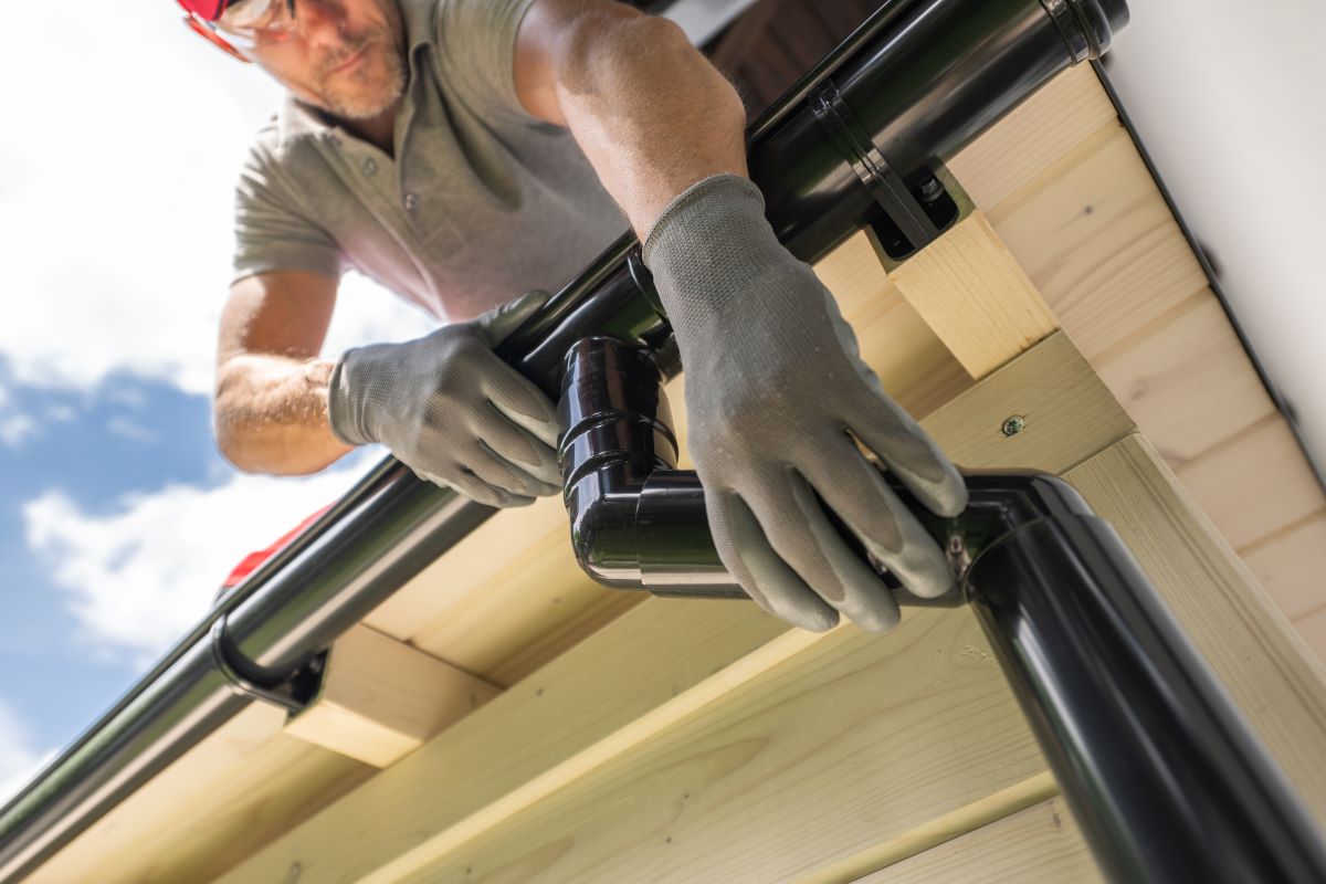 Worker installing a black rain gutter on roof.