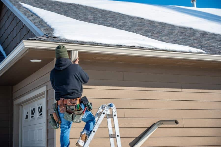 Worker installing gutter on snowy roof