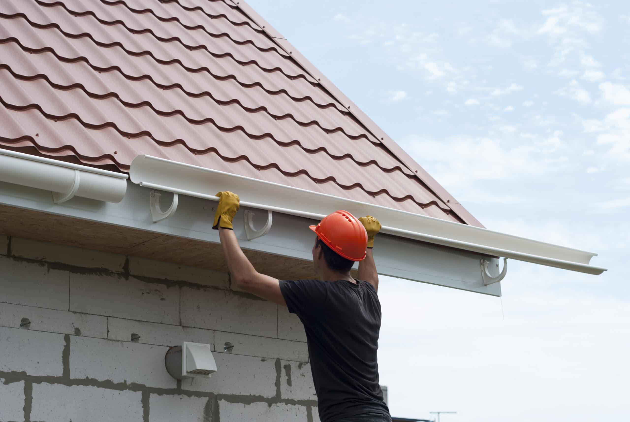 Installer hanging a new white gutter below a tile roof