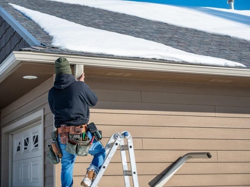 Worker installing gutter on snowy roof